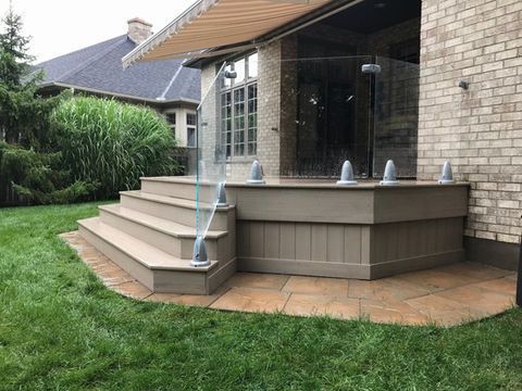 A deck with stairs and a glass railing in front of a brick house.