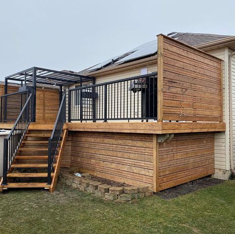 A wooden deck with stairs leading up to it is in the backyard of a house.