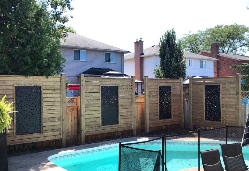 Wooden fence with decorative panels surrounds a swimming pool in a backyard.