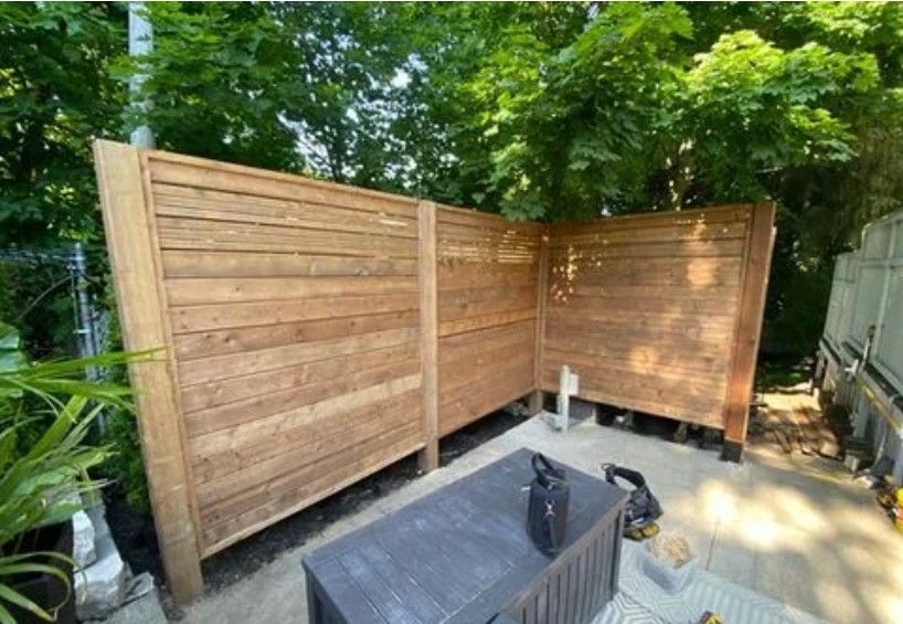 Wooden privacy fence in a backyard, partially enclosing a patio with a dark table.