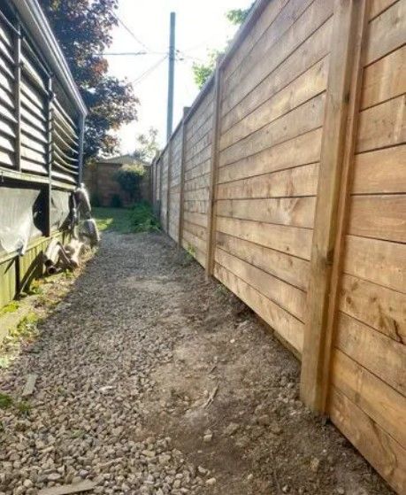 Gravel pathway between a wood fence and building with siding. Bright natural light.