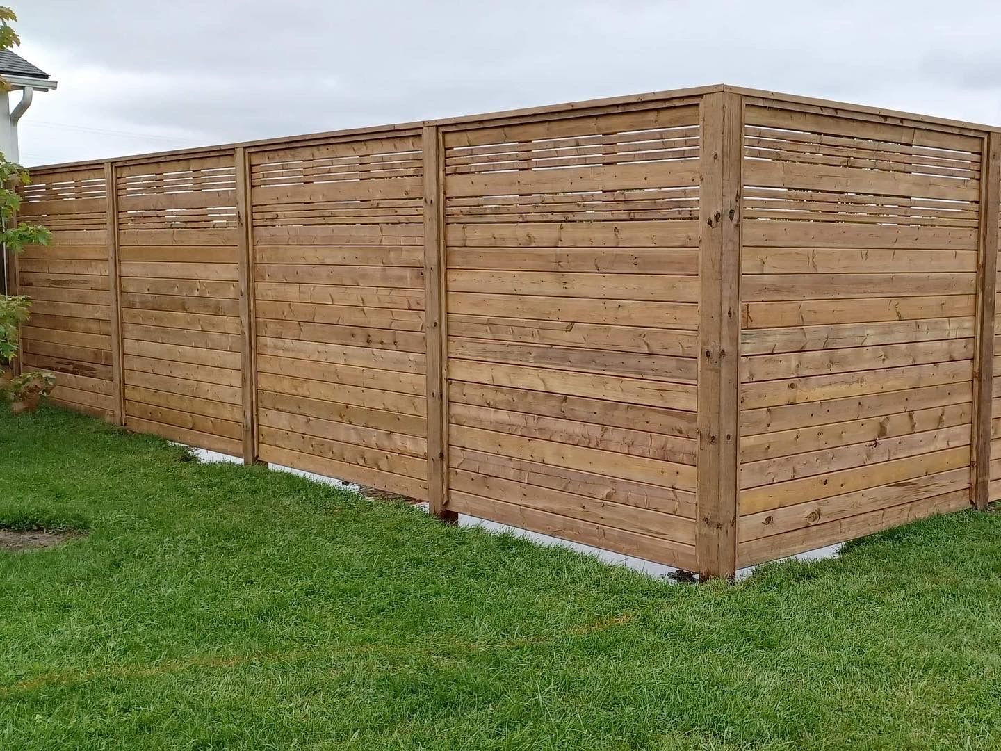 Wooden privacy fence on green grass. Brown wood with a latticework top.
