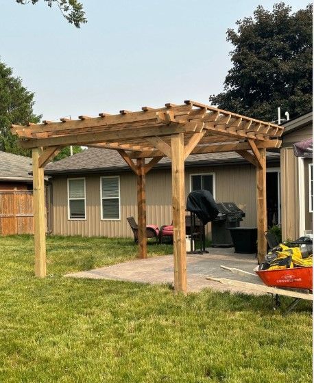 Wooden pergola over a patio in a backyard with grass and a house.