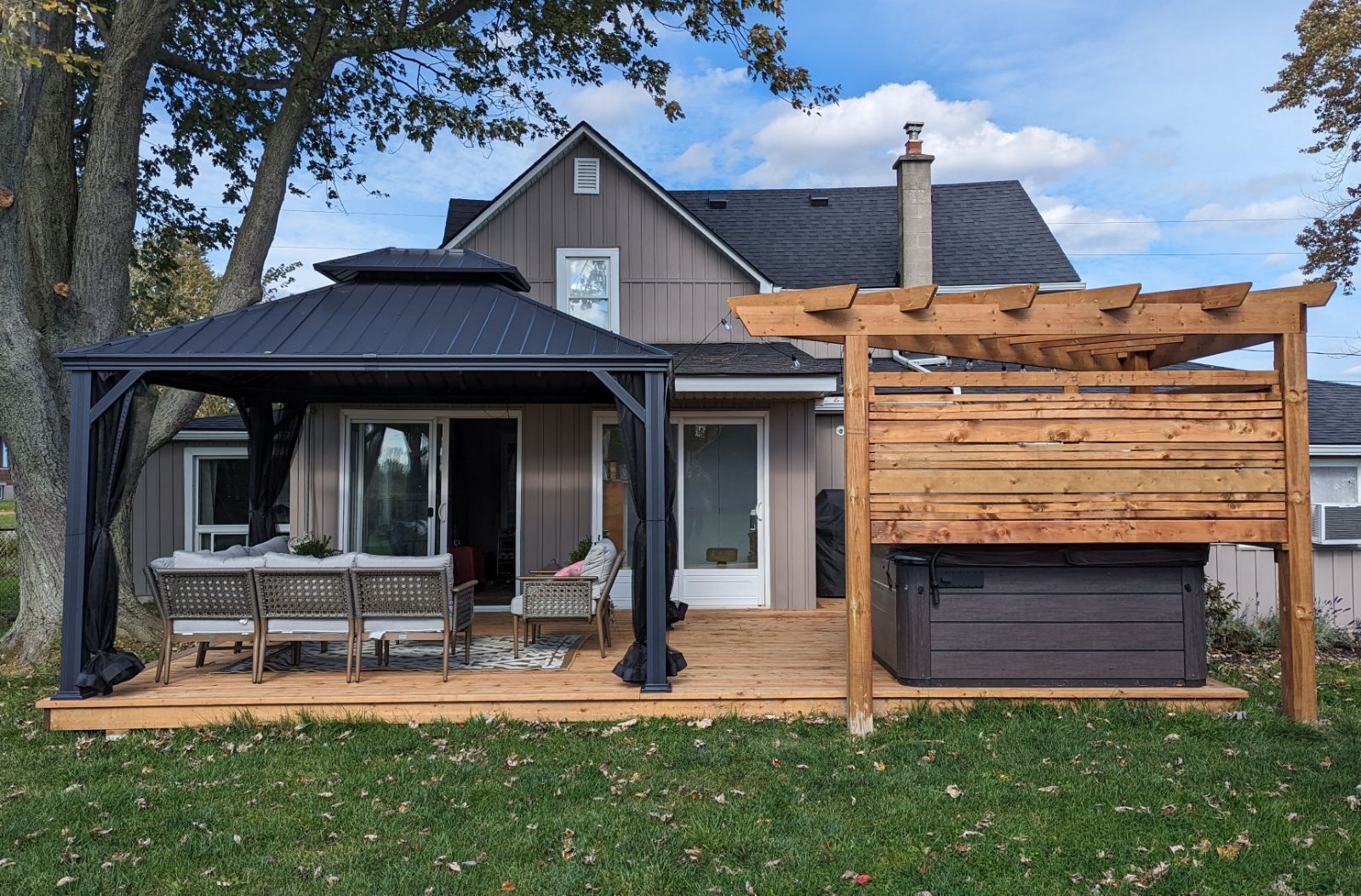 Backyard deck with a gazebo, hot tub, and a two-story gray house.