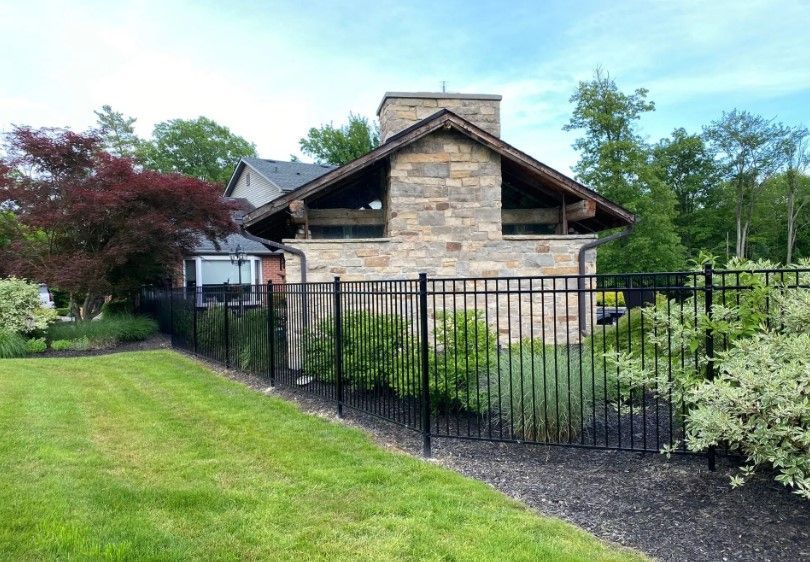 A stone building with a chimney is enclosed by a black metal fence on a green lawn.