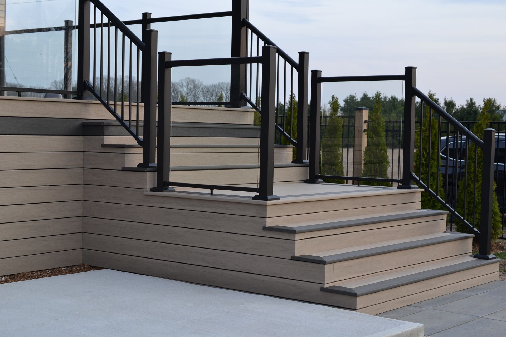 Composite deck stairs with black metal and glass railings.