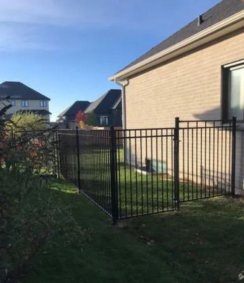 Black metal fence near a beige brick house, surrounding a grassy area.