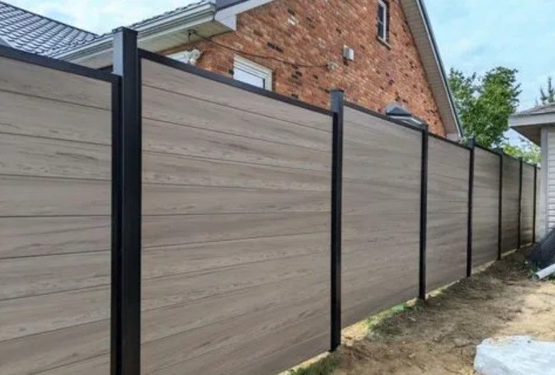 Brown and black privacy fence in front of a brick house.