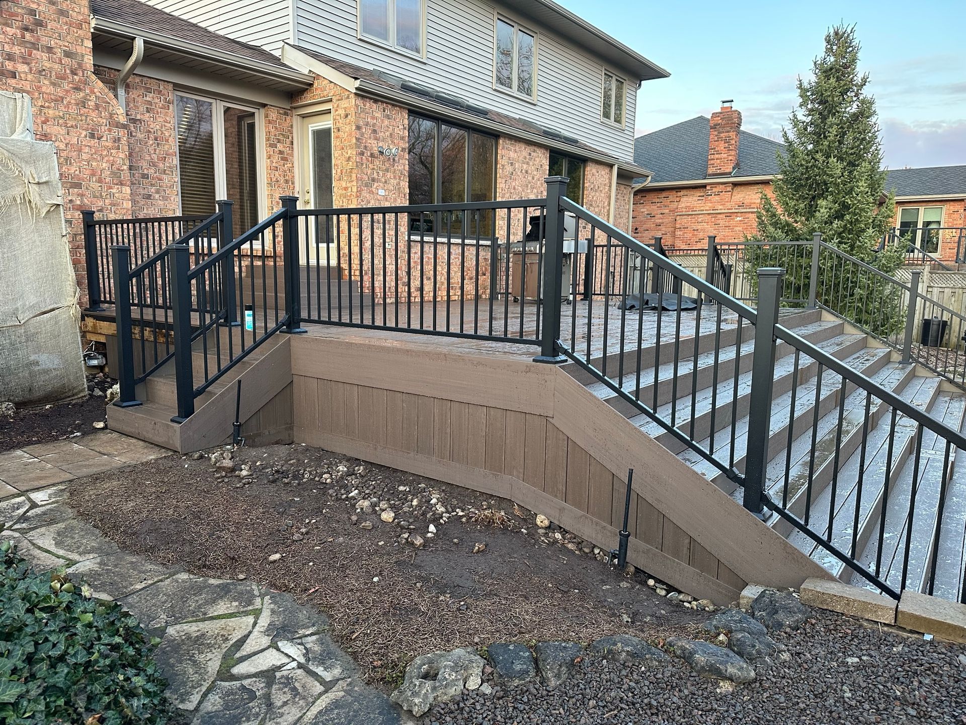 A brick house with a deck and stairs with a black railing.