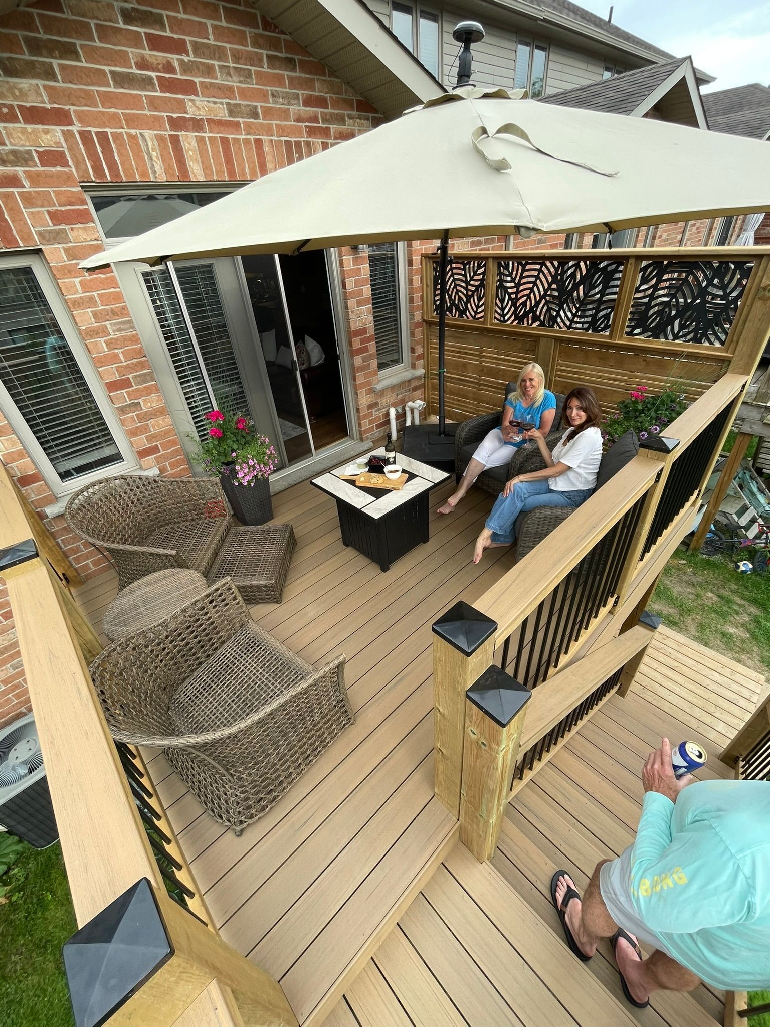 Backyard patio deck with wicker chairs, umbrella, and three people sitting around a fire table