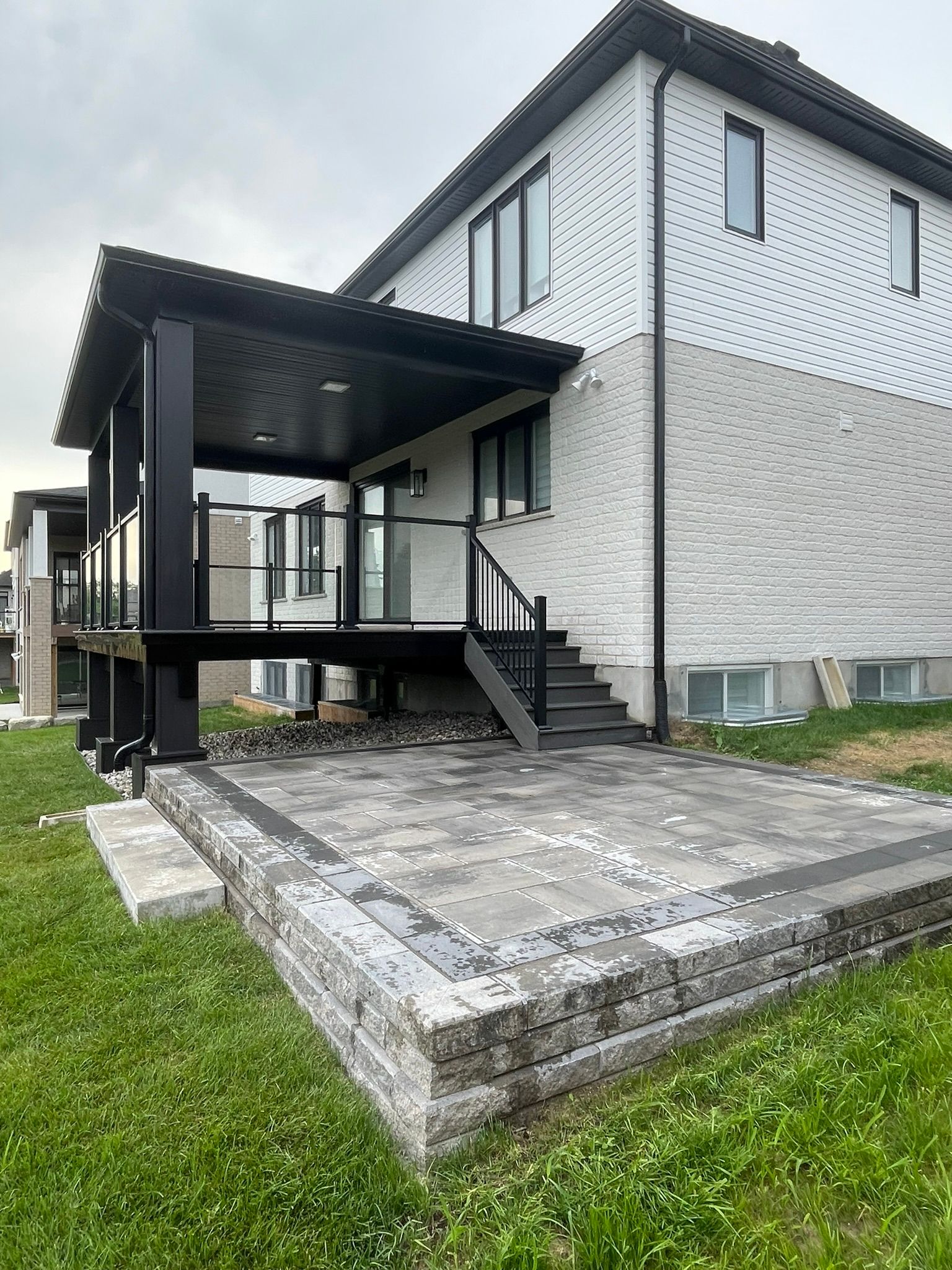 Back of a modern house with a black deck and patio, surrounded by green grass.