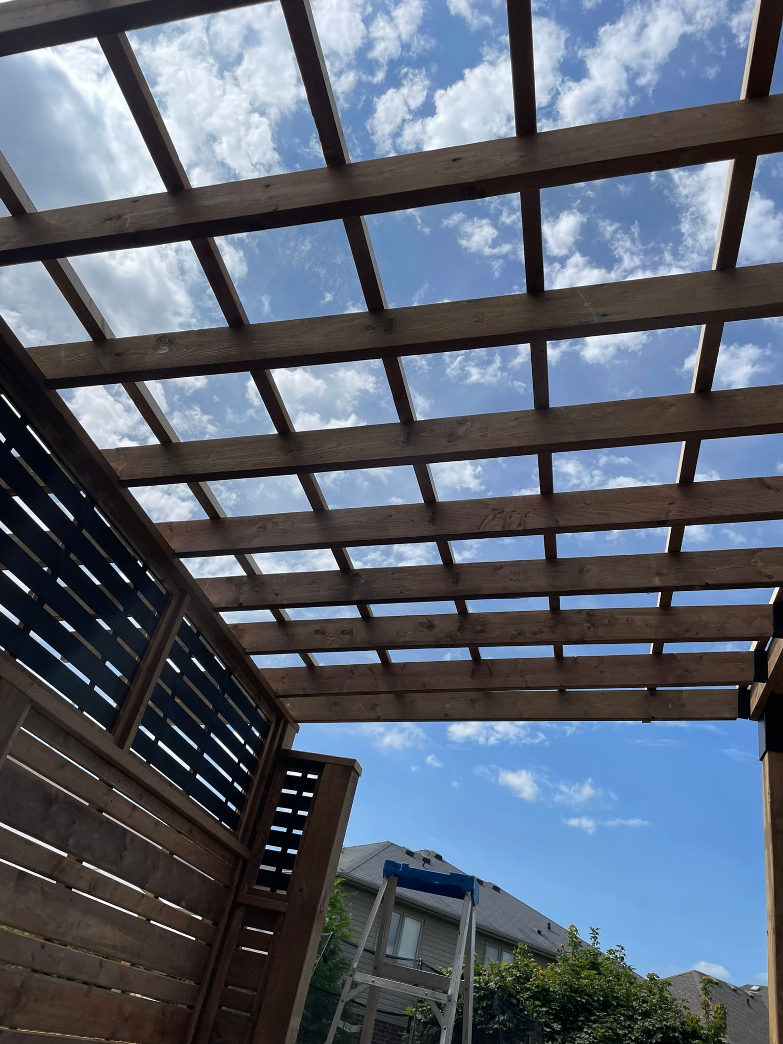 Wooden pergola and privacy fence against a blue sky with clouds.