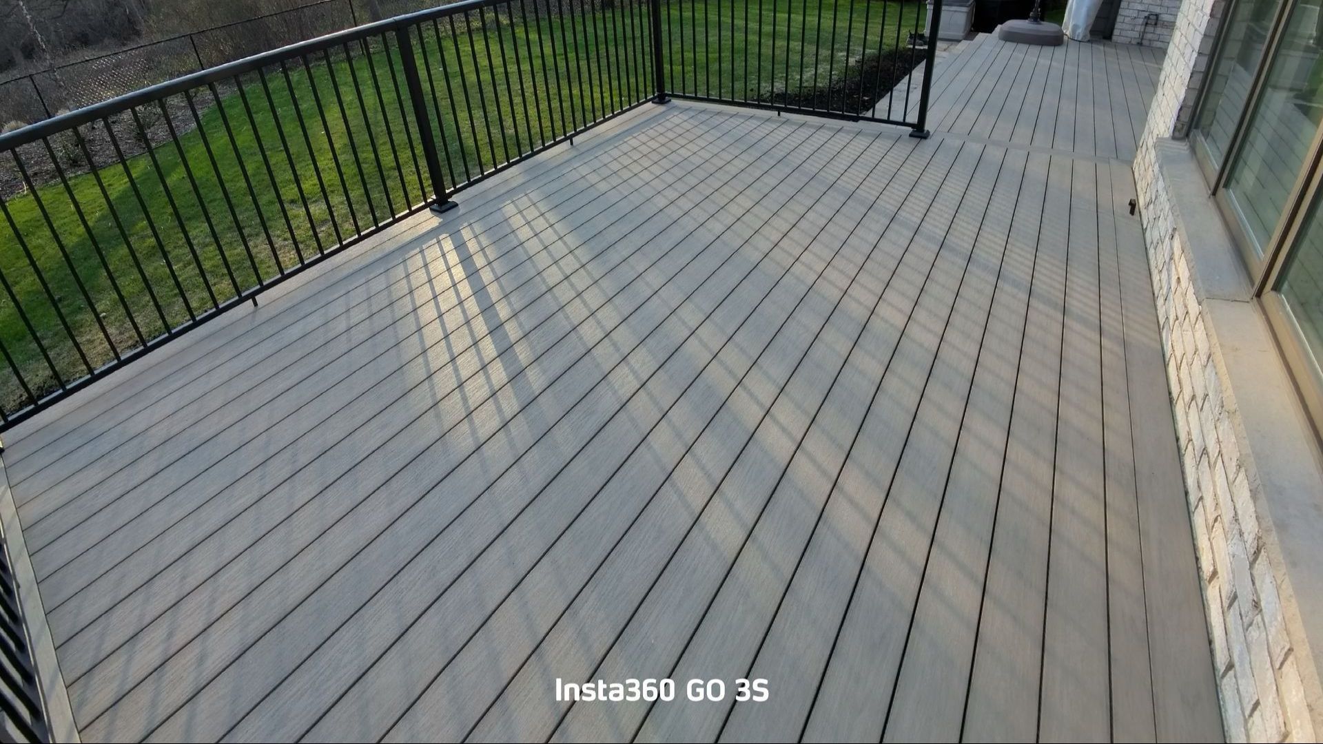 Gray wooden deck with black railing overlooking a green lawn.