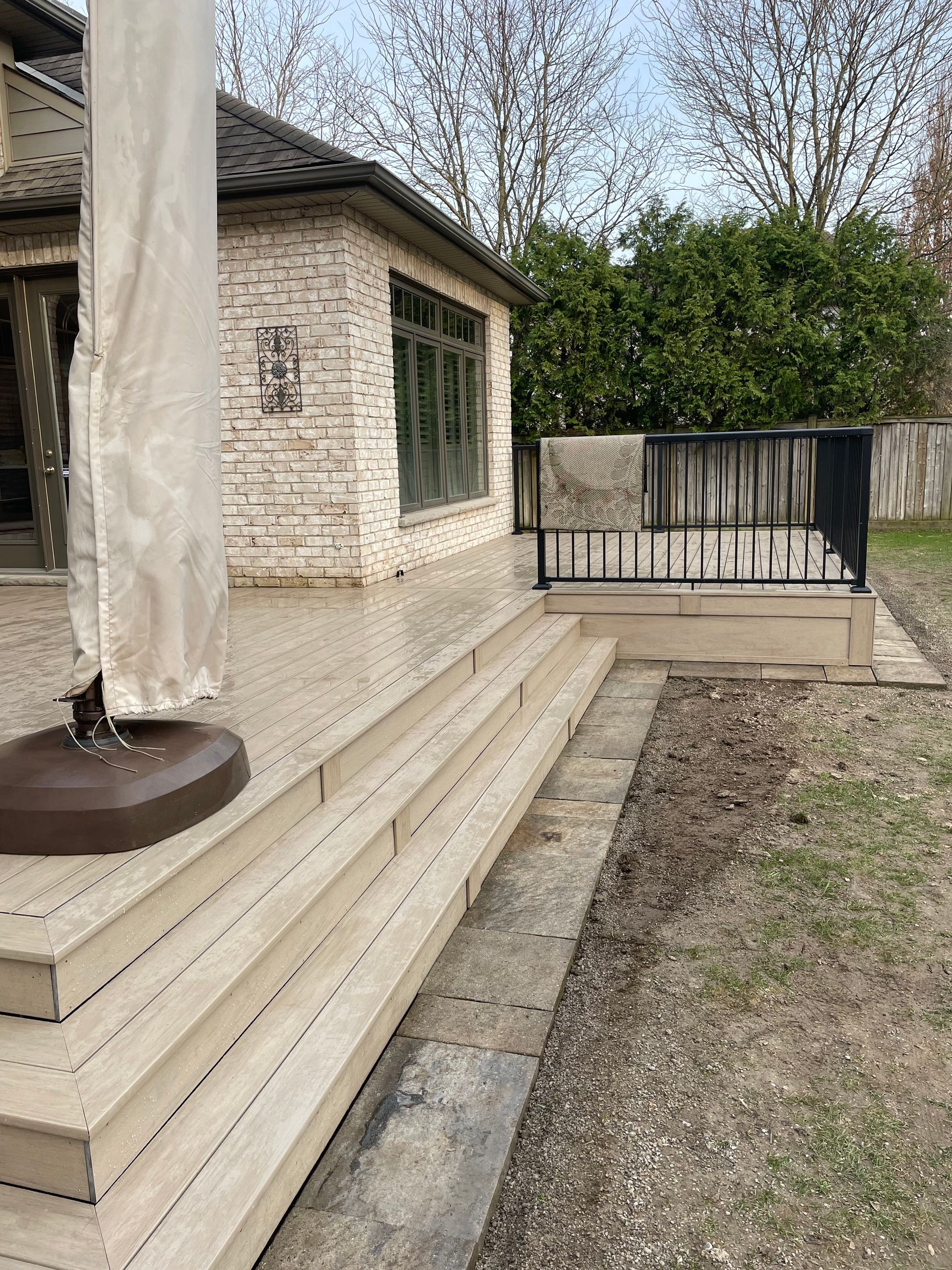 A wooden deck with stairs and an umbrella in front of a house.