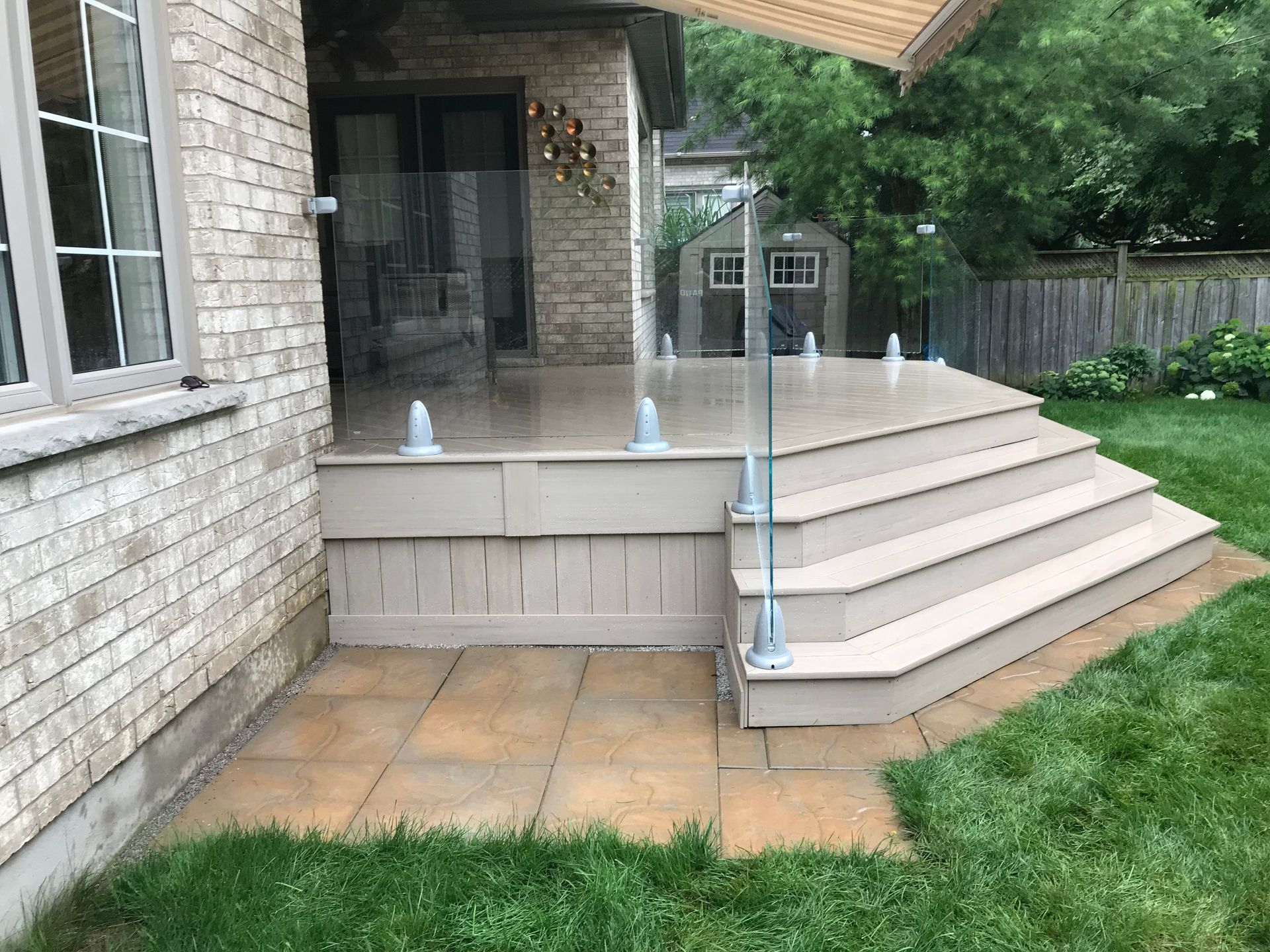 A deck with stairs and a glass railing in front of a brick house.