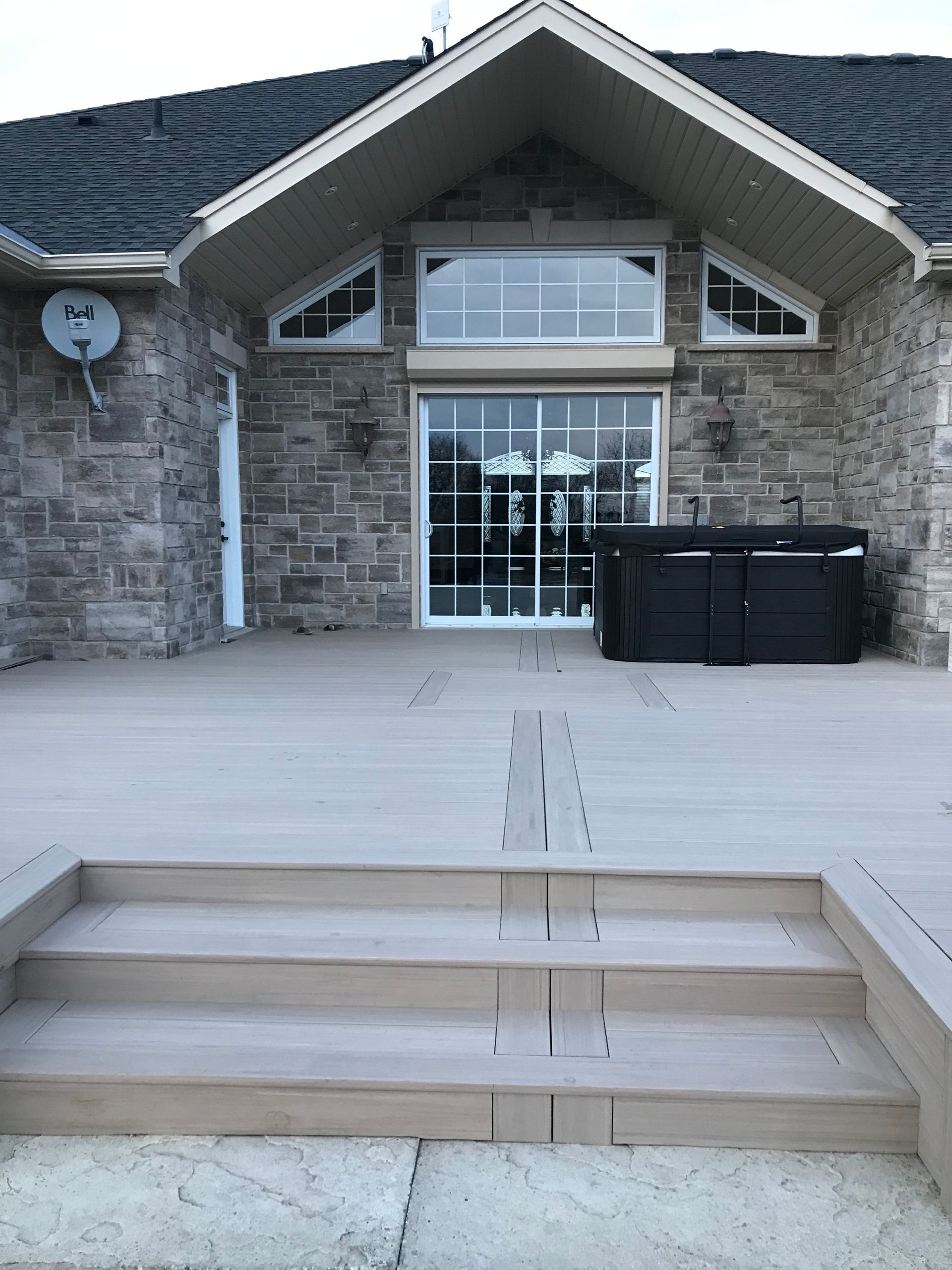 A wooden deck with steps leading to a house with large windows and stone siding.