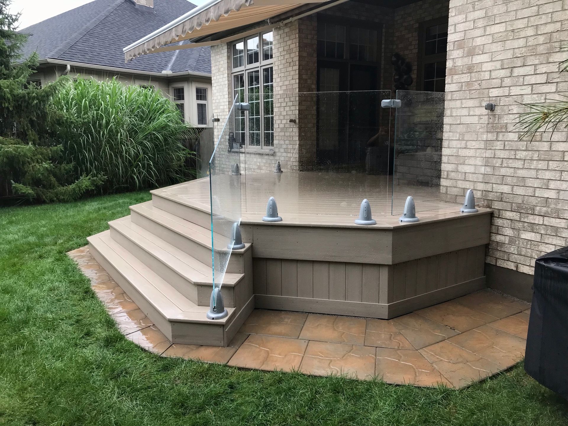 A deck with stairs and a glass railing in front of a brick house.