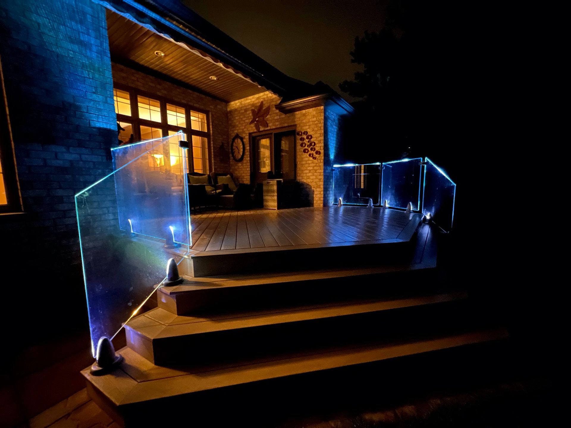 A deck with stairs and a glass railing is lit up at night.