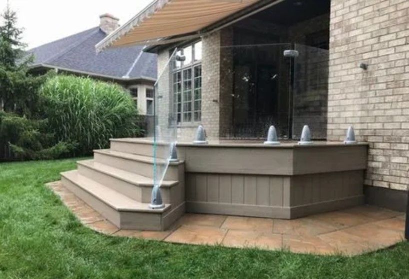 Outdoor patio with steps, glass railing, and awning. Brown brick building. Green lawn.