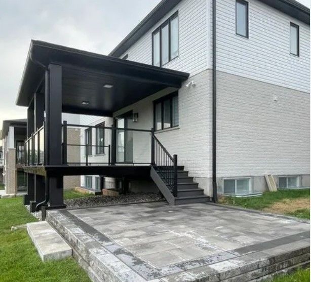 Black deck with glass railings and stairs, connected to a two-story white house with brick accents.
