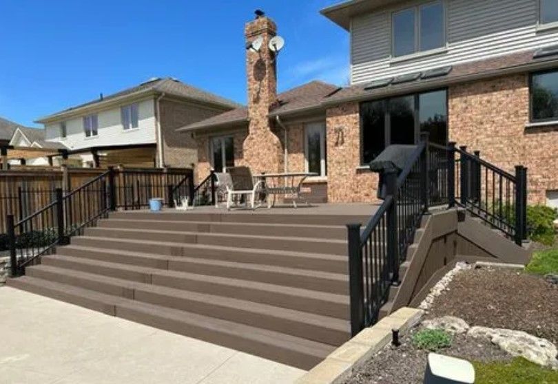 Brown tiered deck with black railing outside brick house, sunny day.
