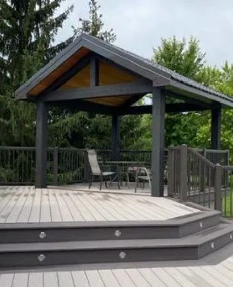 Gray gazebo on a wooden deck with seating, steps, and built-in lights, set in a natural, outdoor environment.