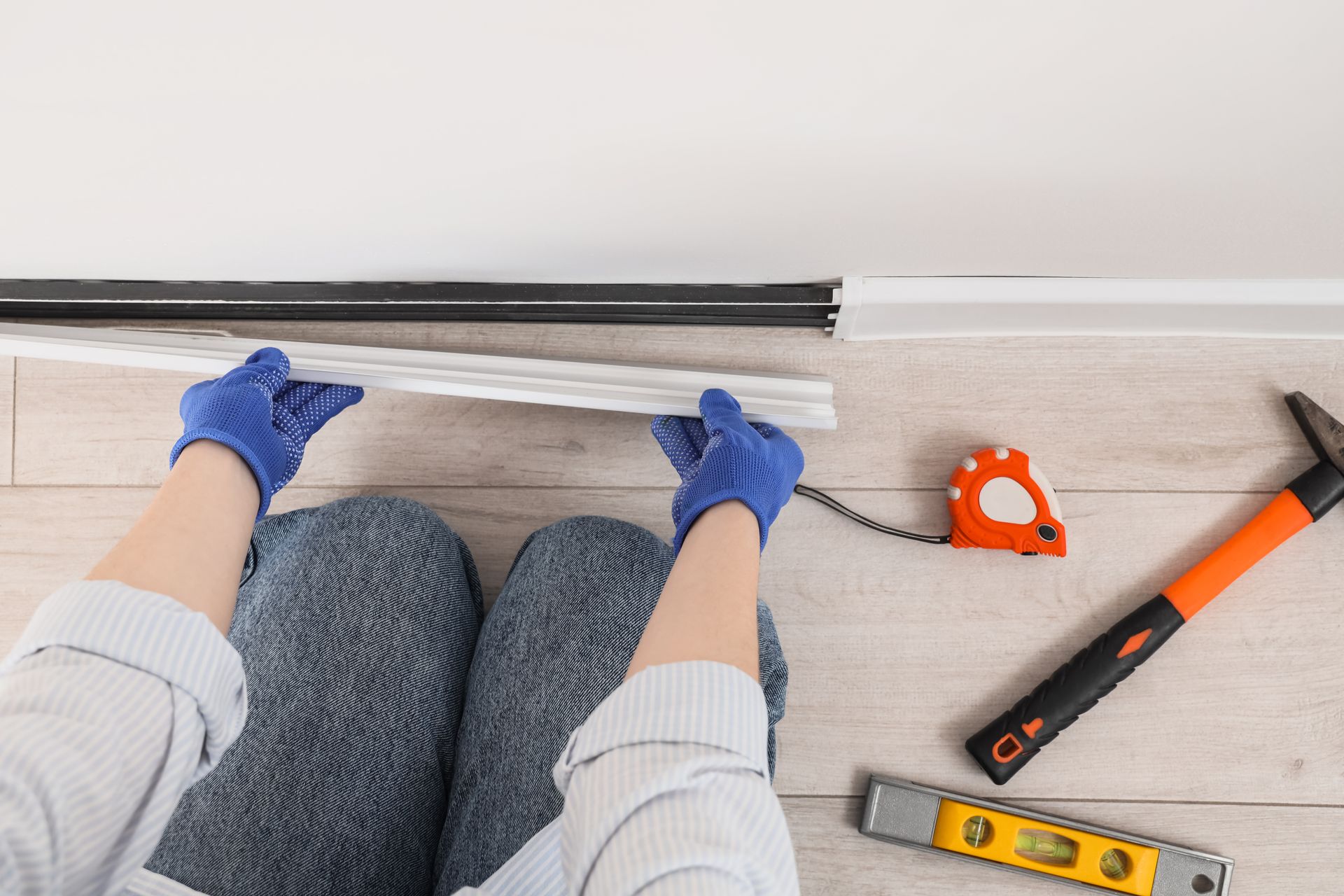 Person installing a floor track with blue gloves, tools nearby on a light wood floor