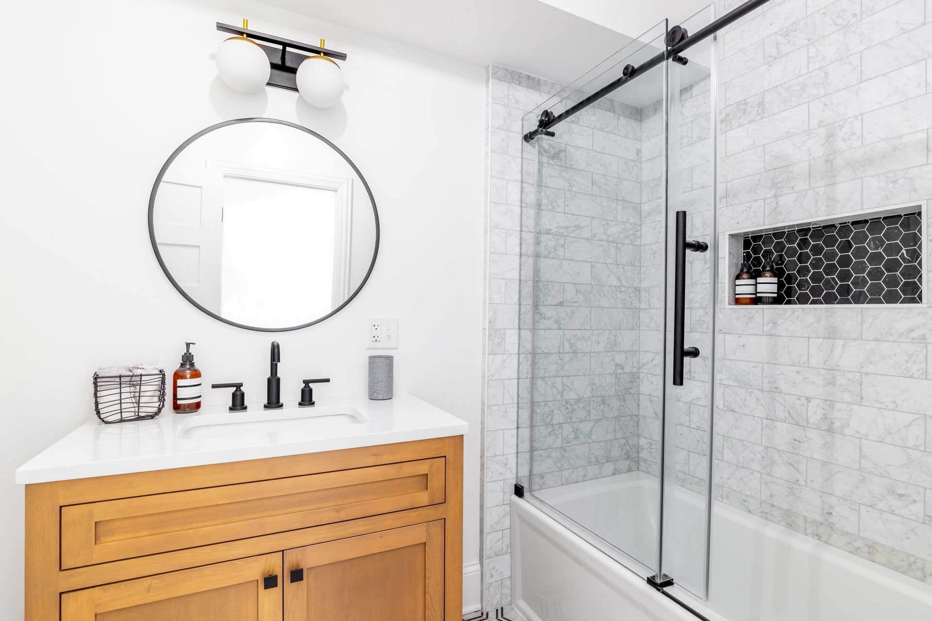 Bright modern bathroom with wood vanity, round mirror, and glass shower.