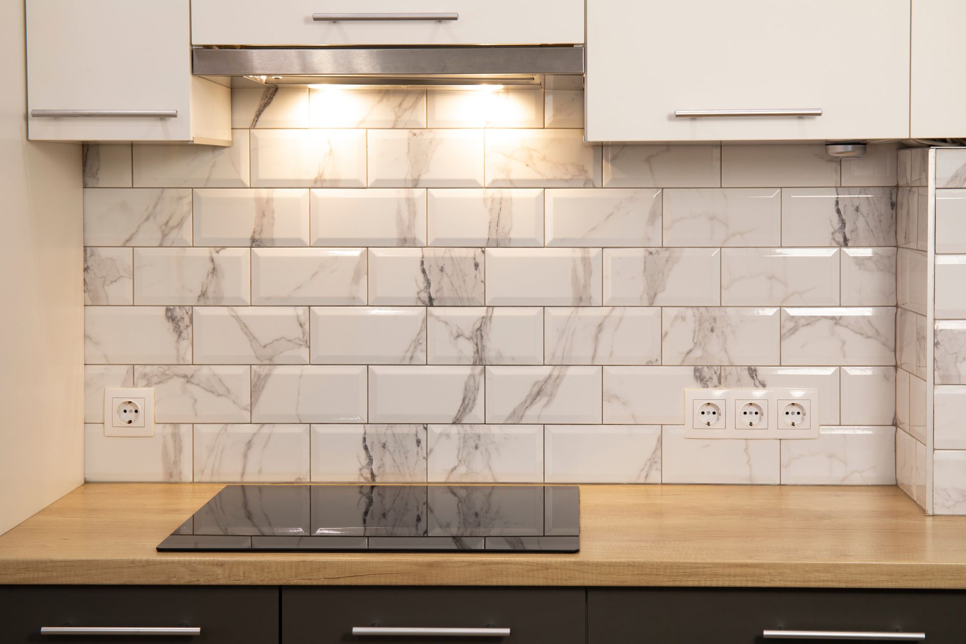 Modern kitchen backsplash with white subway tiles, under-cabinet lighting, and a black cooktop on a wood countertop
