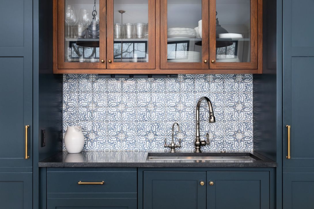 Navy blue kitchen cabinets with brass handles, wood glass-front uppers, and a patterned tile backsplash with sink.