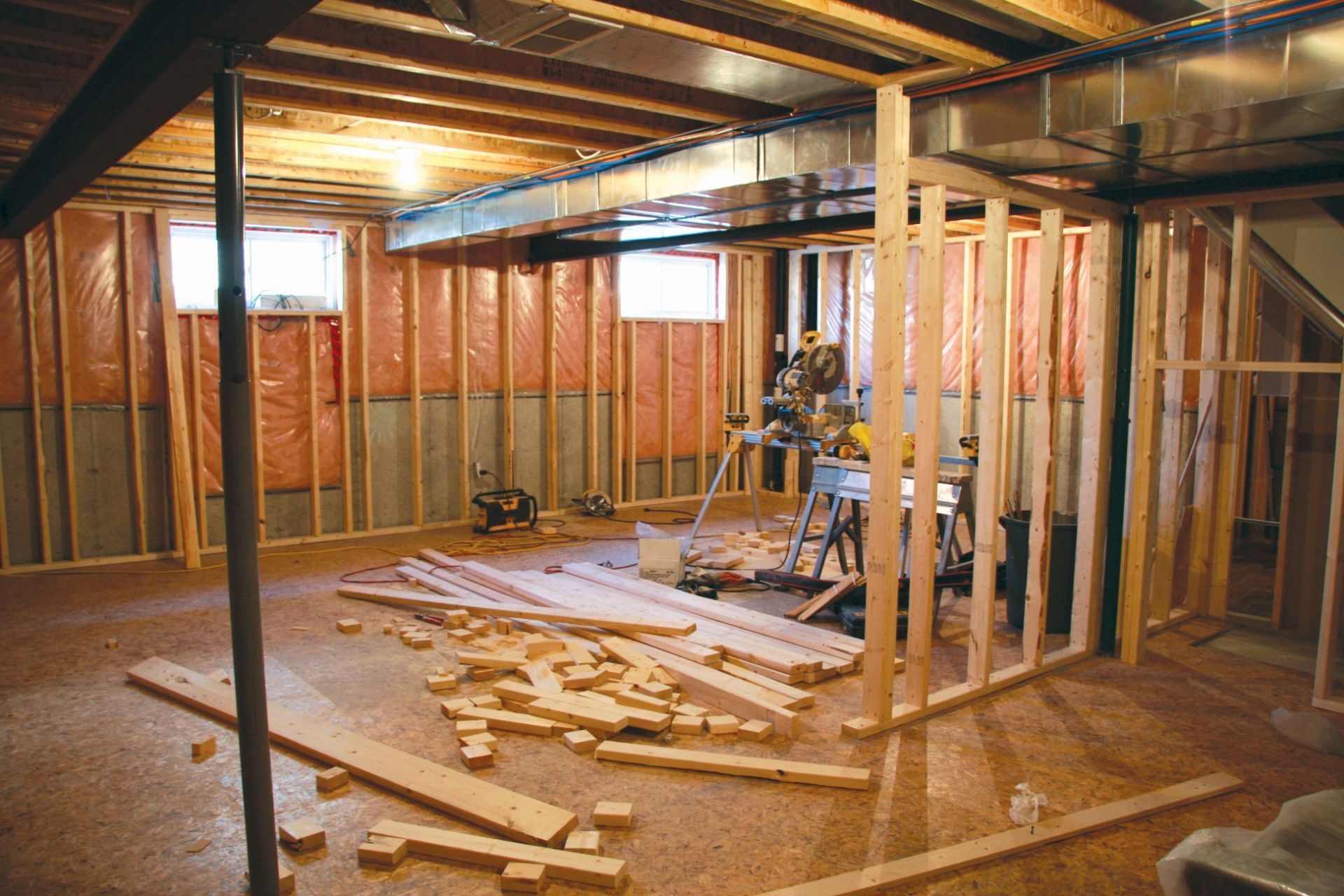 Basement under construction with exposed studs, beams, tools, and scattered lumber on the floor
