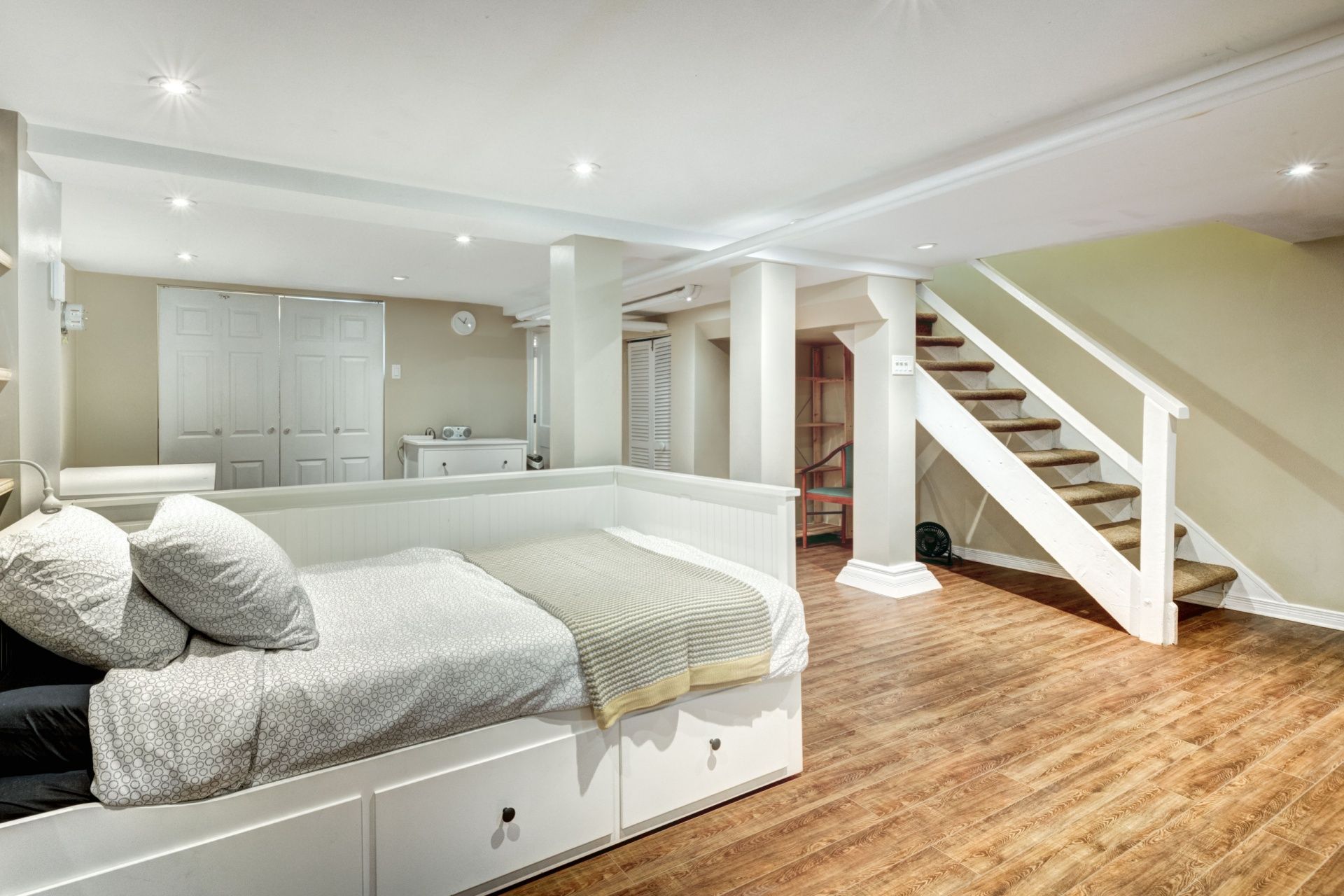 Bright basement bedroom with twin beds, white stairs, and hardwood floor
