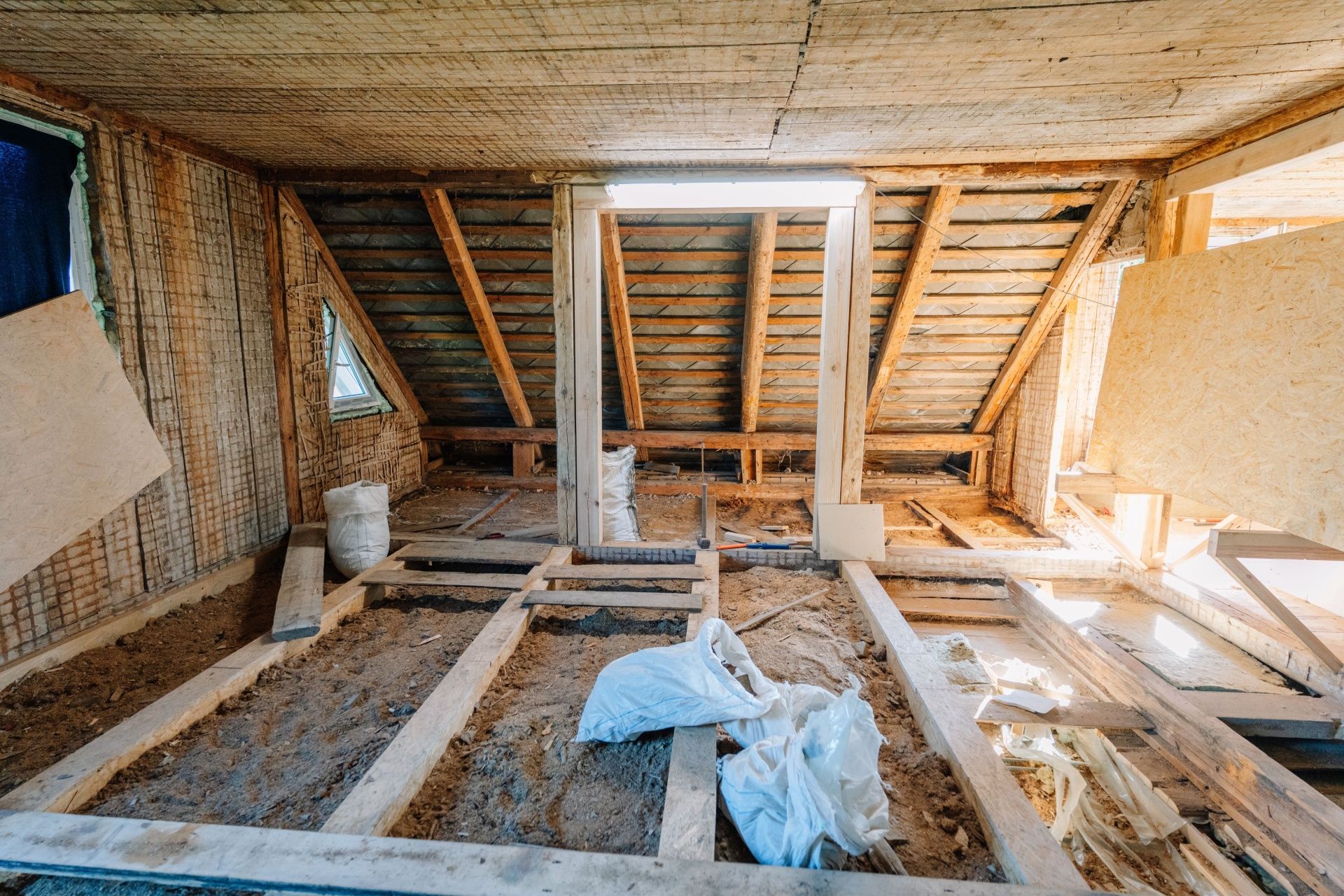 Attic under renovation with exposed wooden beams, insulation, and construction debris on the floor