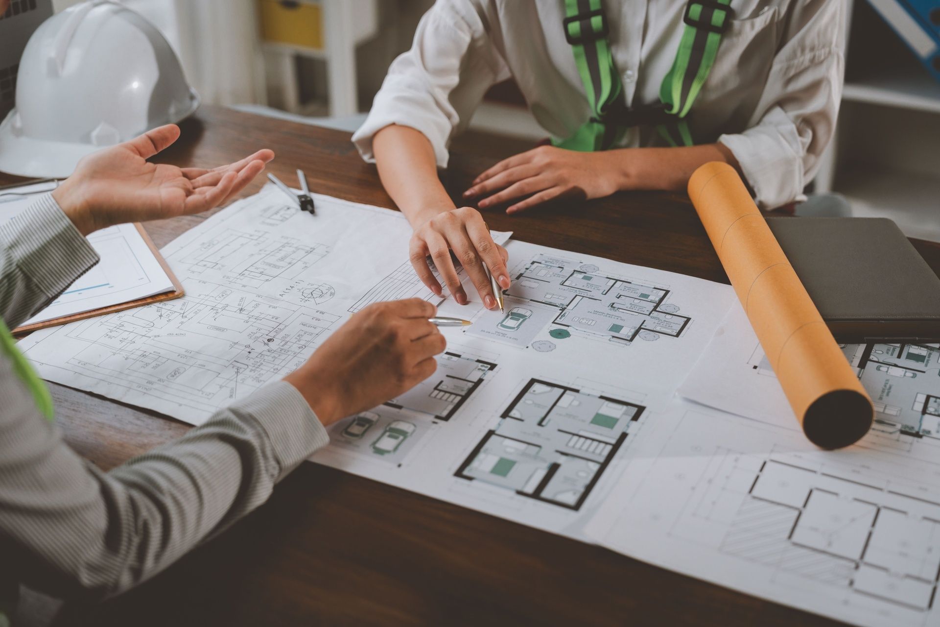 People reviewing architectural floor plans on a desk with pencils and rolled drawings.