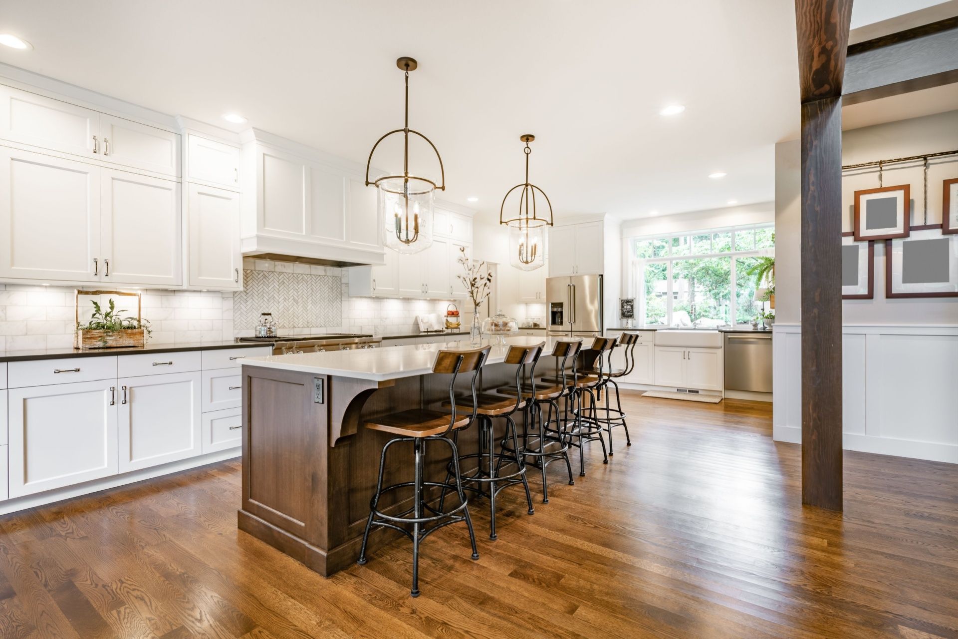 Bright white kitchen with island, barstools, wood floors, and pendant lights