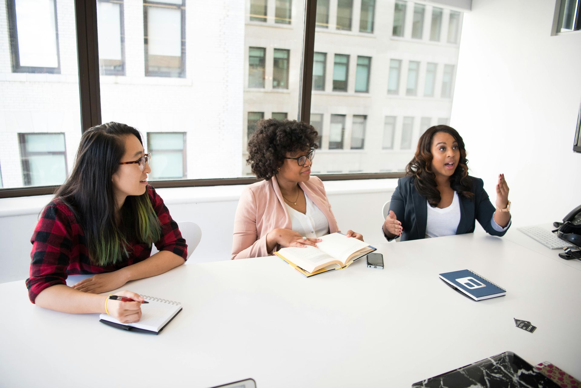 Three women are sitting at a table in a conference room having a meeting.