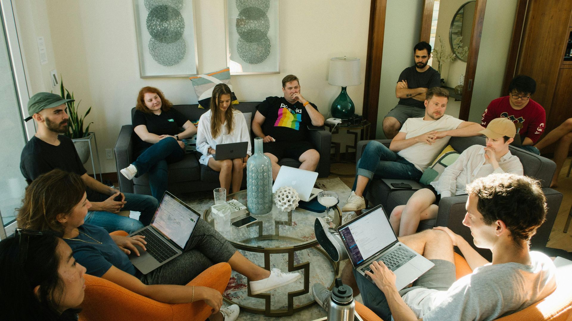 A group of people are sitting around a table with laptops in a living room.