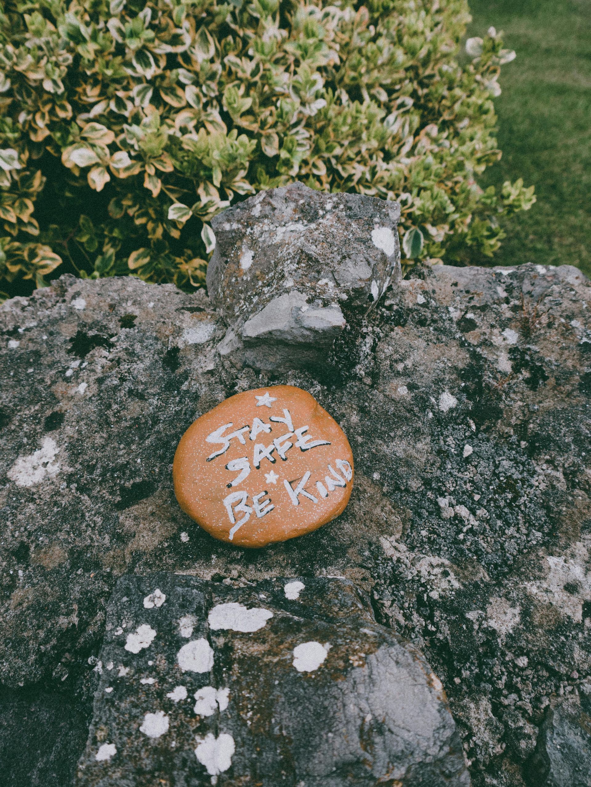 A stone with the words `` stay safe be kind '' written on it is sitting on a rock.