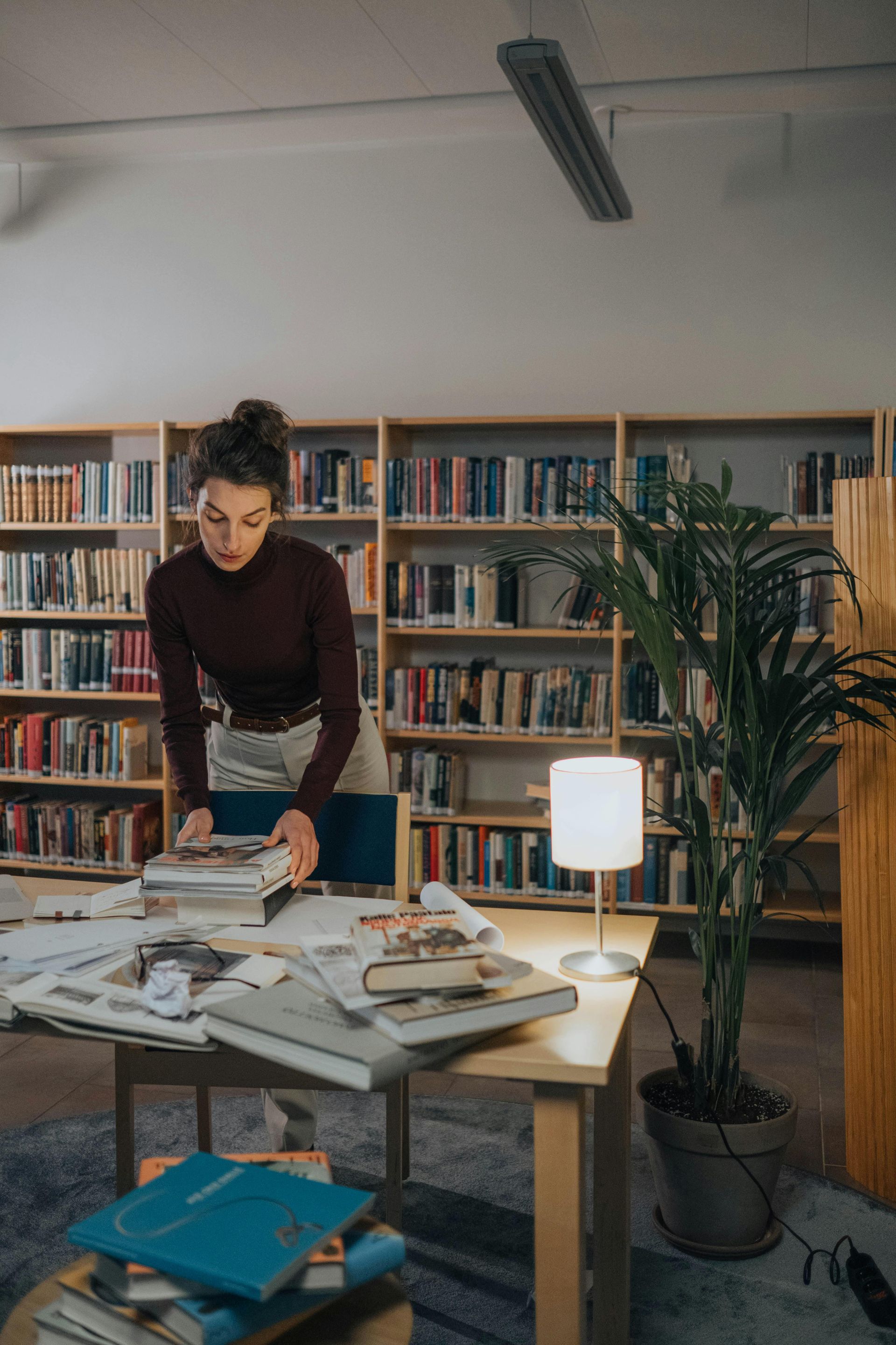 A woman is standing at a table in a library surrounded by books.