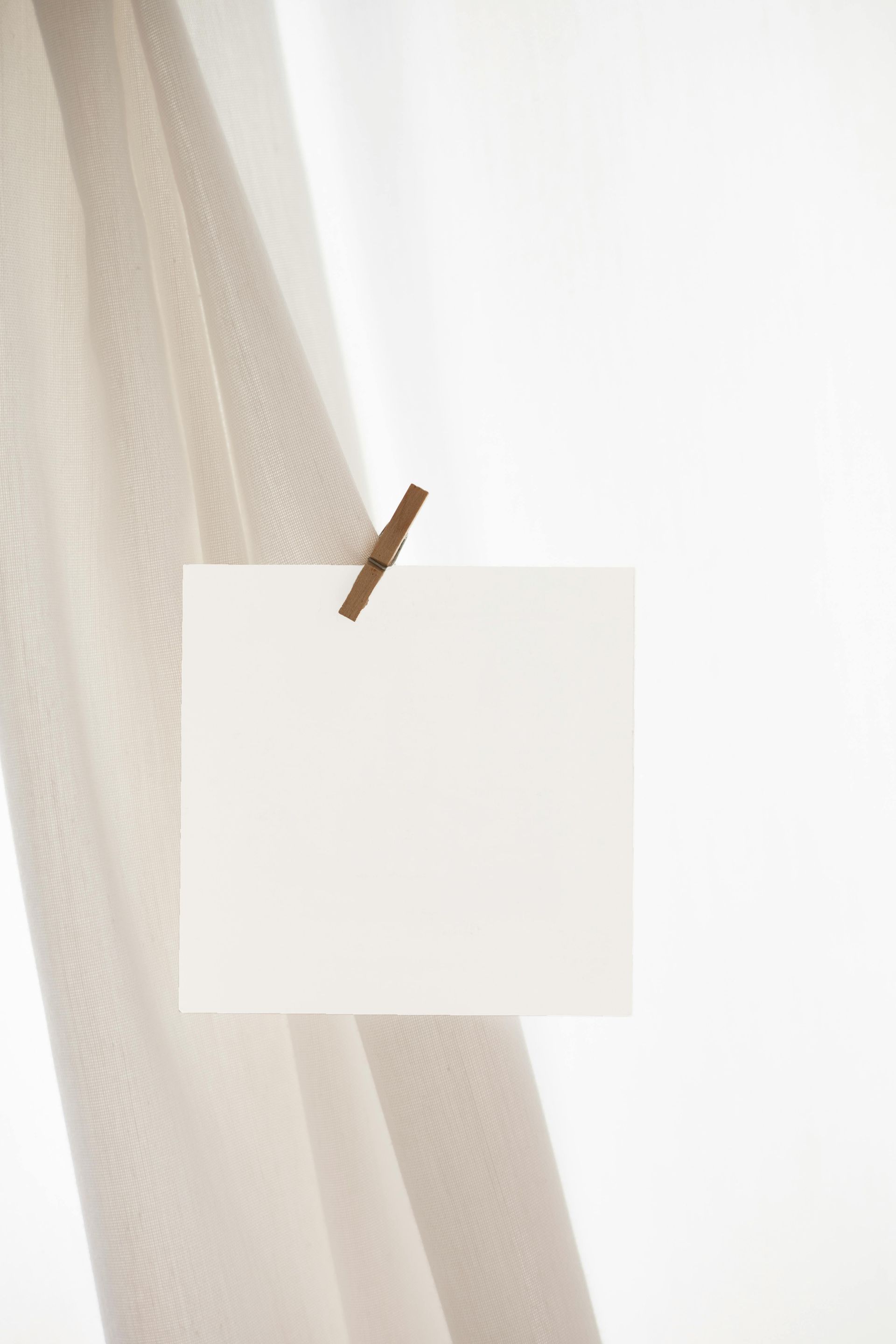 A piece of paper is hanging on a clothespin on a white curtain.