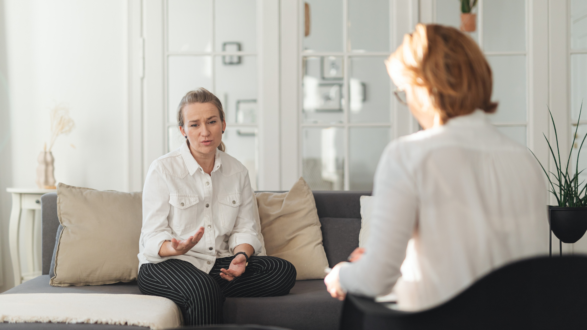 Woman on couch talking to person in chair; therapy session.
