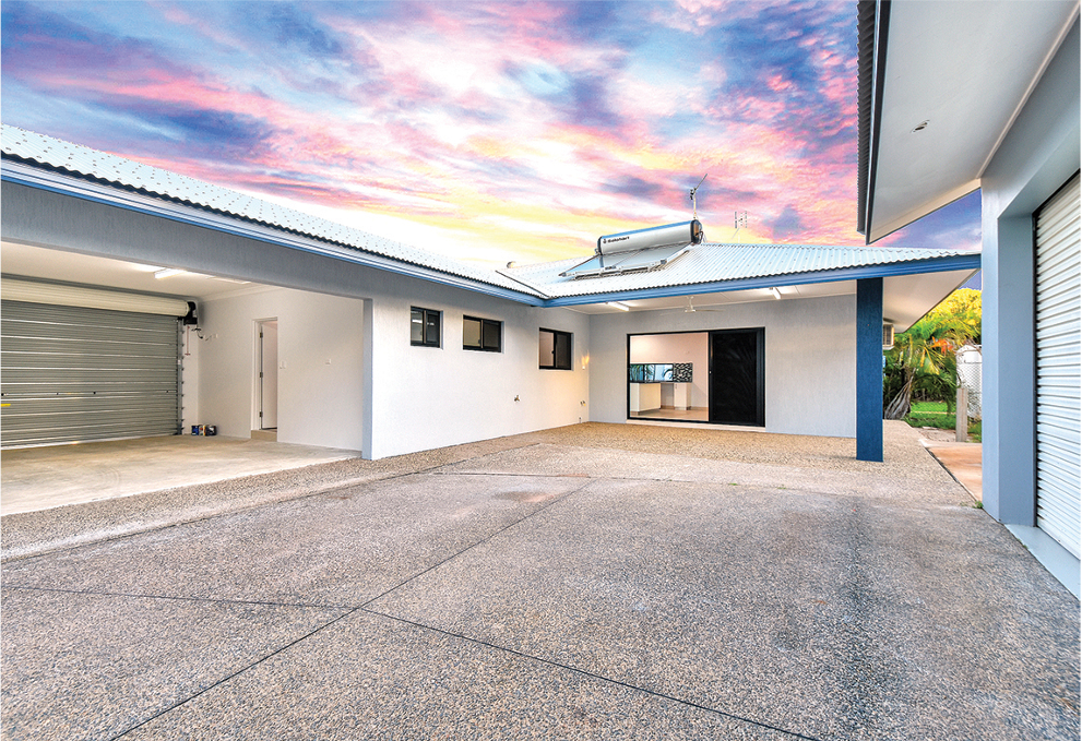 Exterior of a white house with a gray garage door and blue accents, against a colorful sunset.
