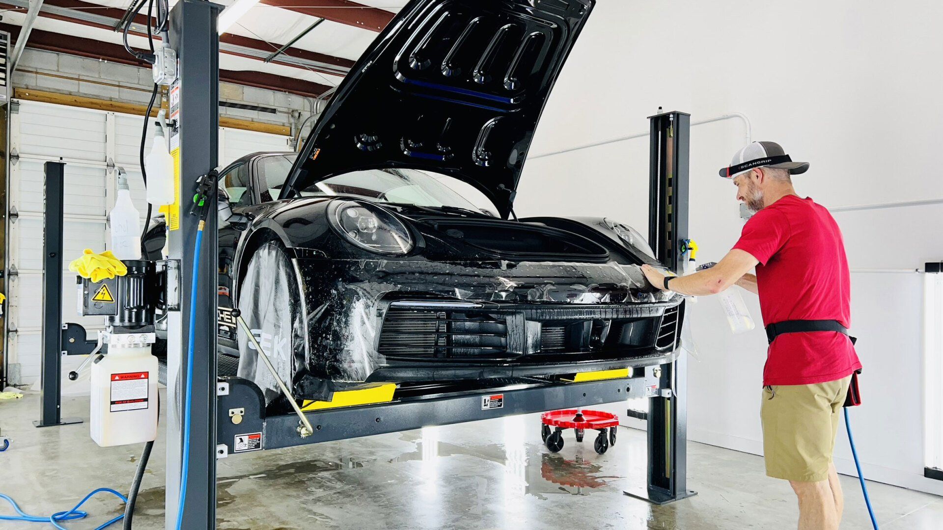 A man is washing a car on a lift in a garage.