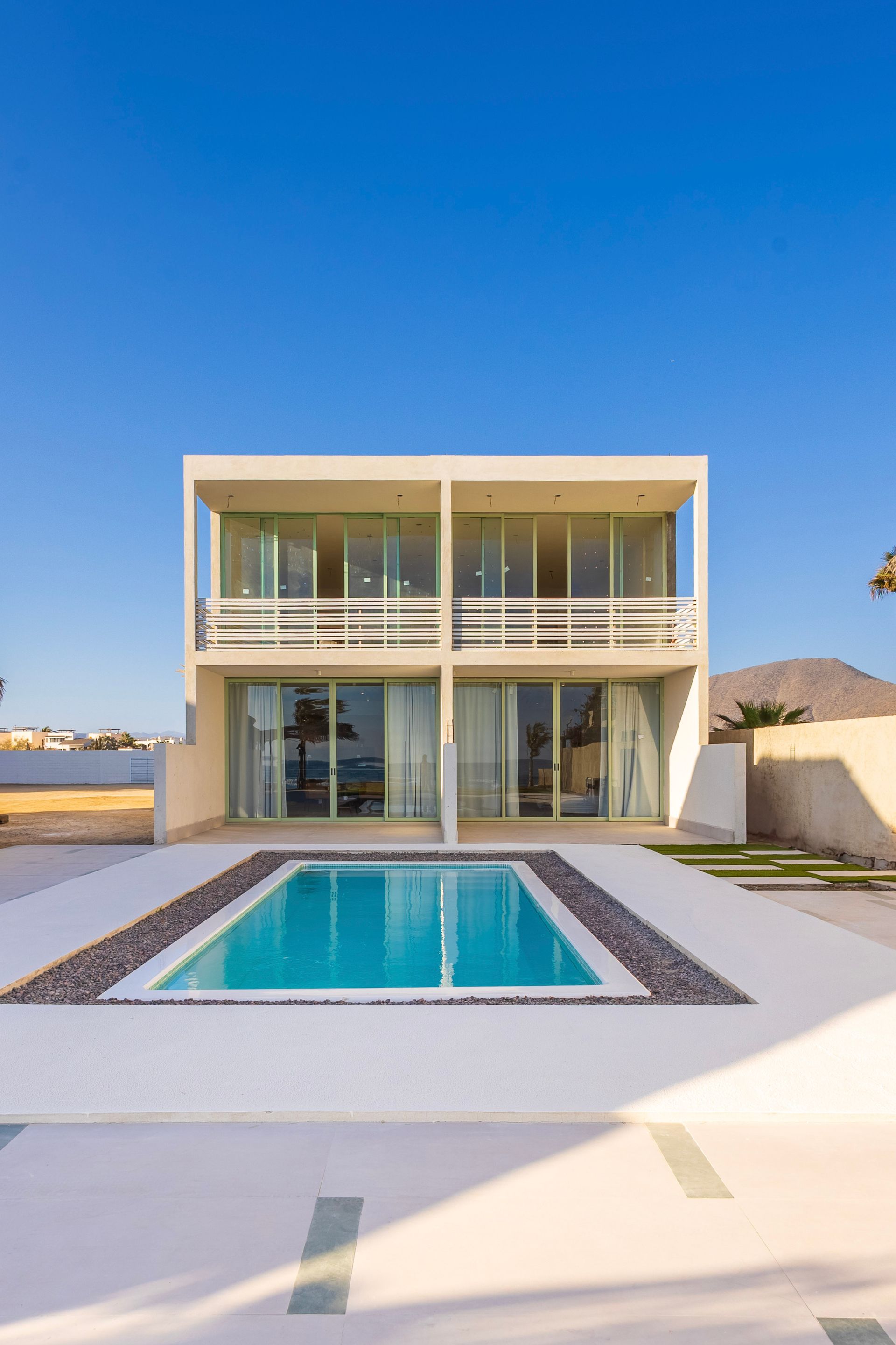 Modern white two-story home with pool, blue sky, and a mountain in the distance.