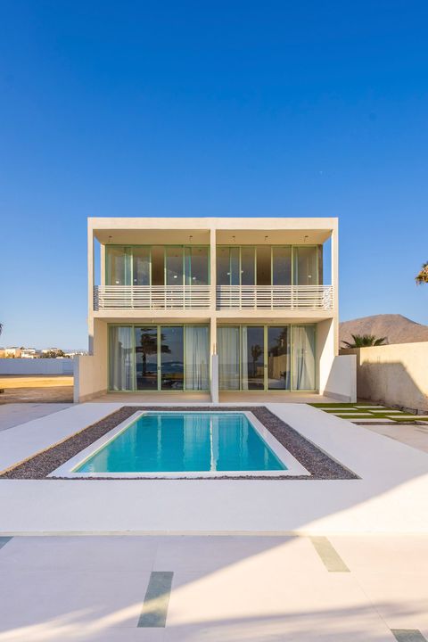 Modern white two-story home with pool, blue sky, and a mountain in the distance.