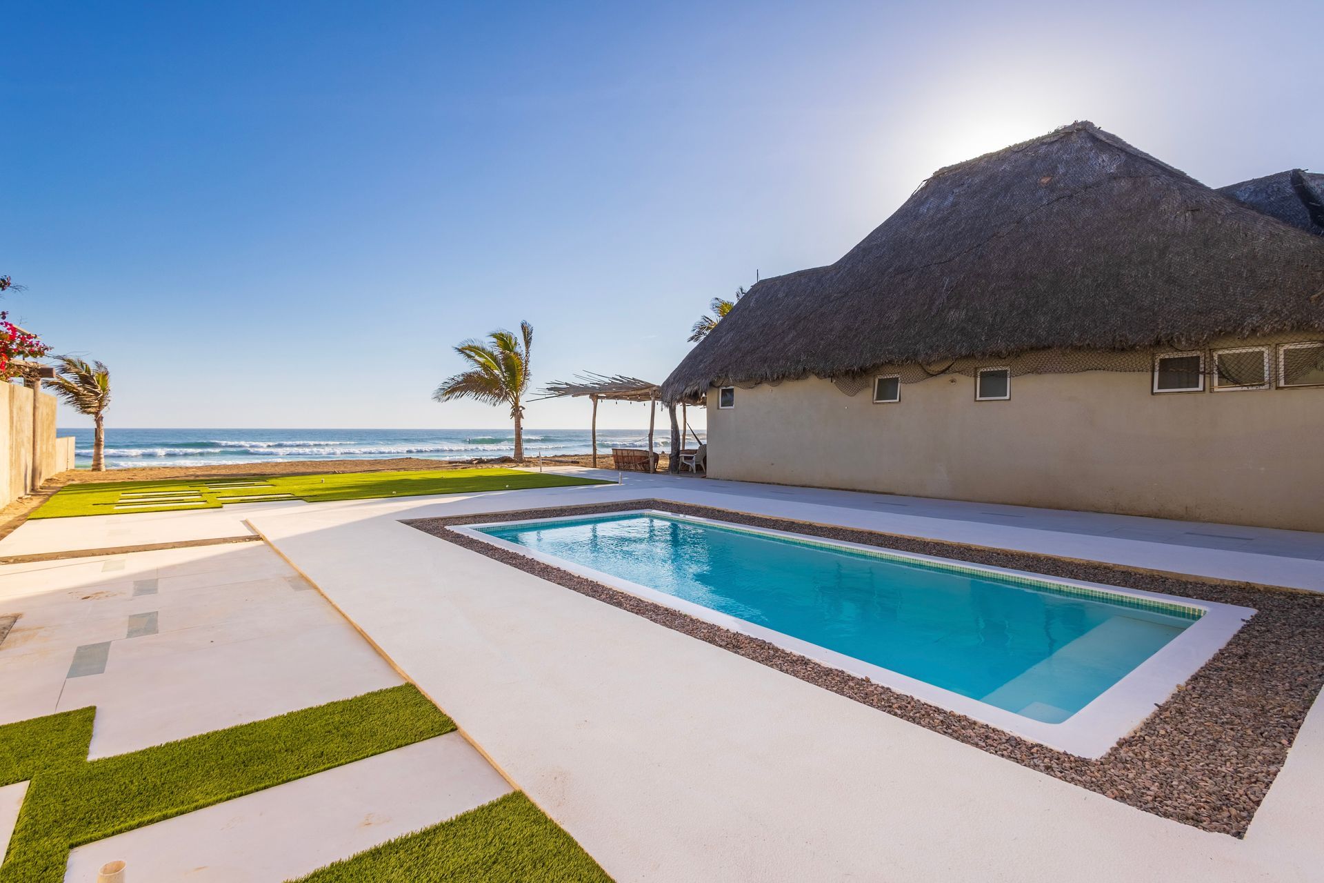 Poolside view of a thatched-roof building and the ocean under a bright blue sky.