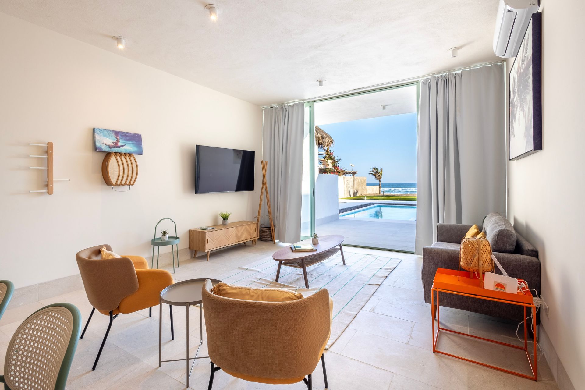 Living room with sea view, featuring tan chairs, gray sofa, coffee table, TV, and pool visible.