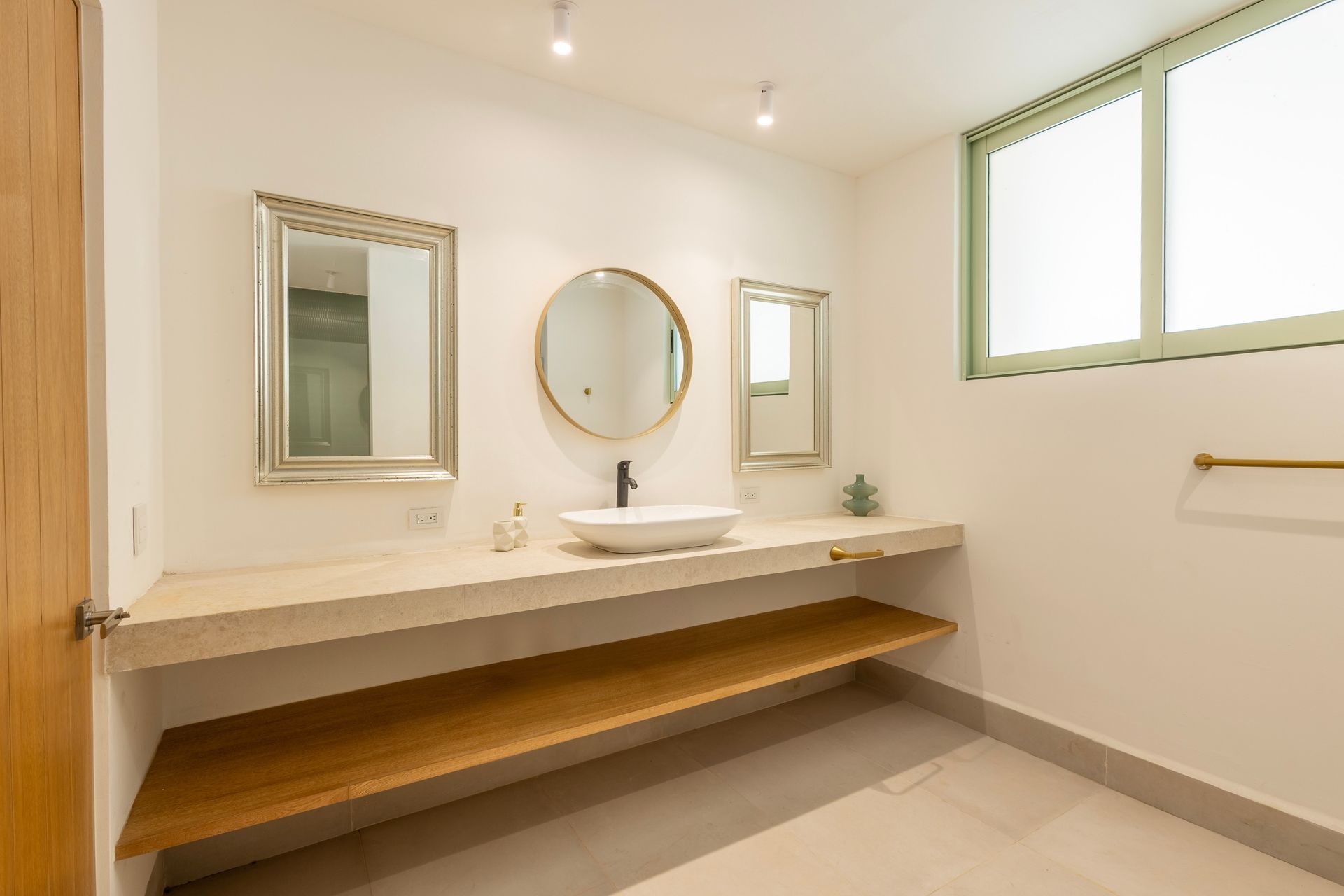 Bathroom with floating shelves and three mirrors above a white sink. Gold and wooden accents.