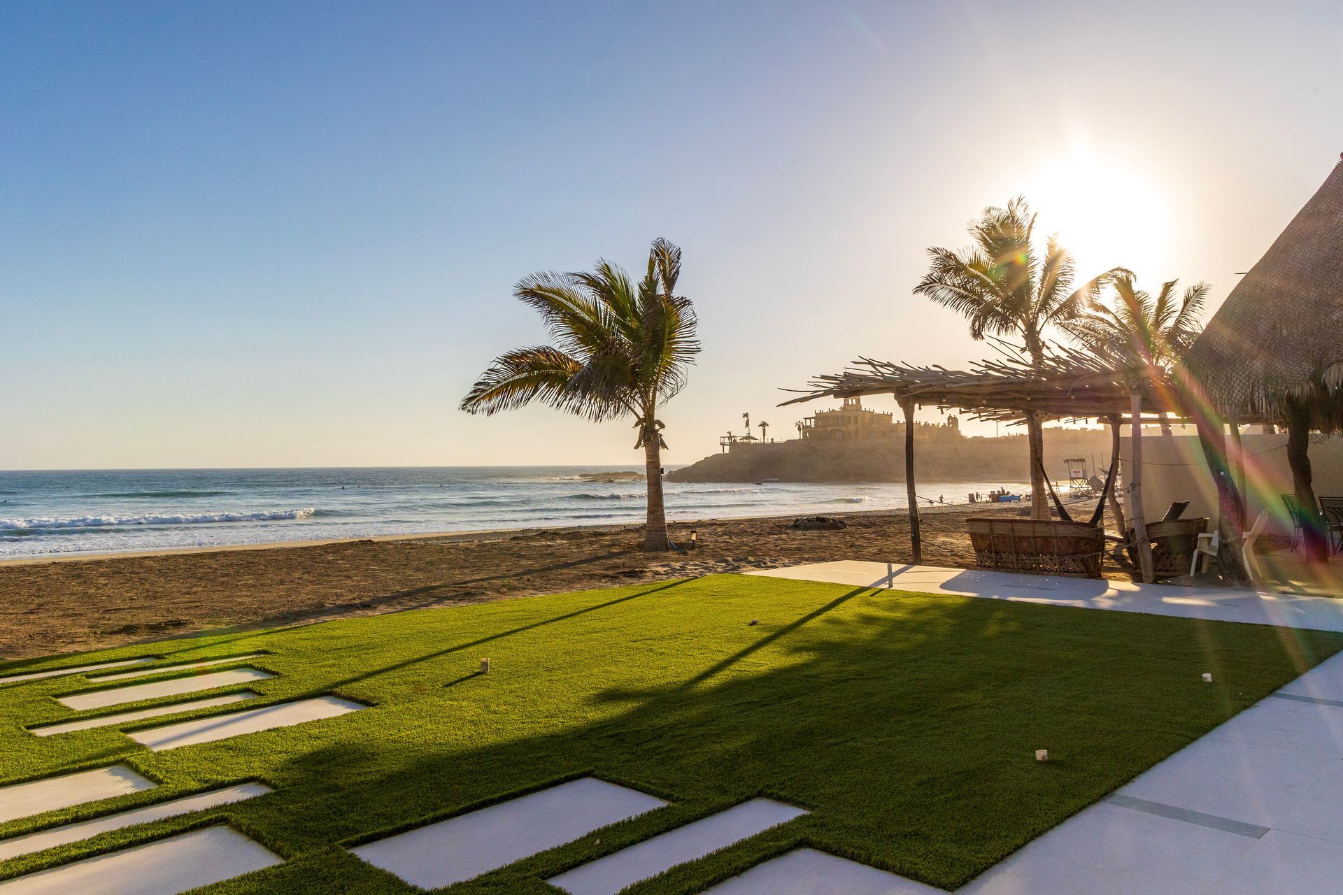 Beachfront with palm trees, grassy area, and ocean under a sunny sky.