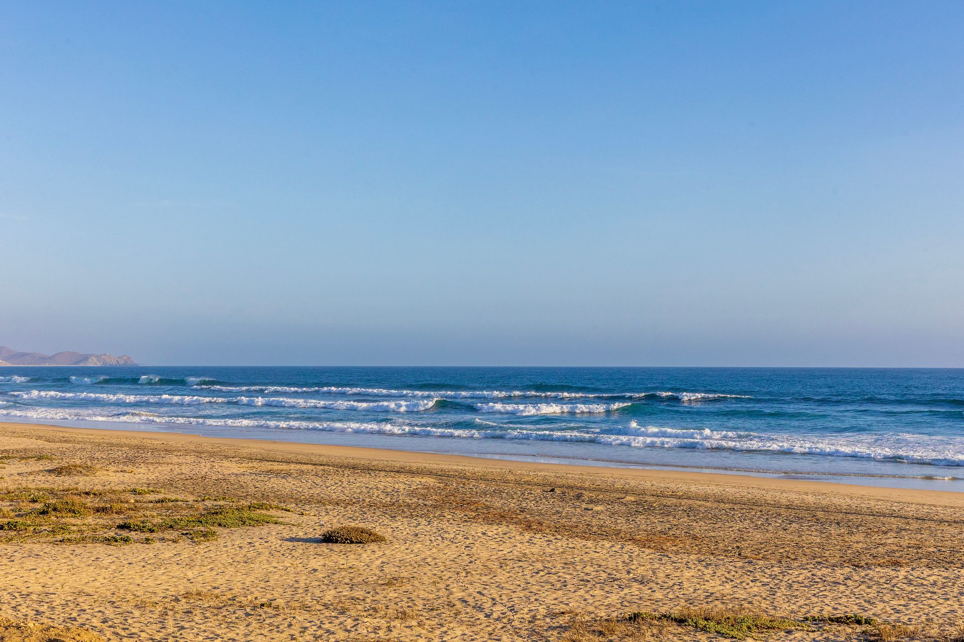 Sandy beach meets the ocean under a clear blue sky.